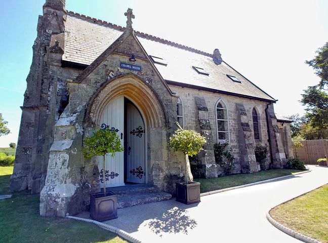 Stone building with arched doorway and gated windows with potted plants at Chapel House in Chale
