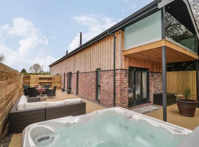 Outdoor patio area with hot tub sofa and dining table next to a brick and wood house at Lugg View in Cross Keys near Hereford