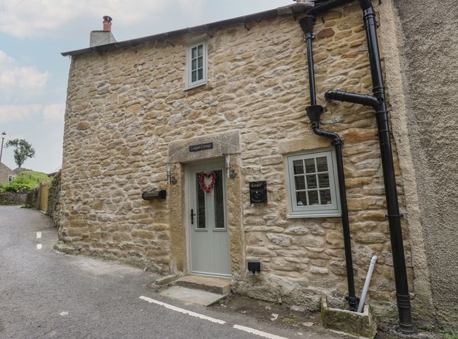 Stone exterior of Lydgate Cottage with a pale door and windows and black drainpipes in Eyam