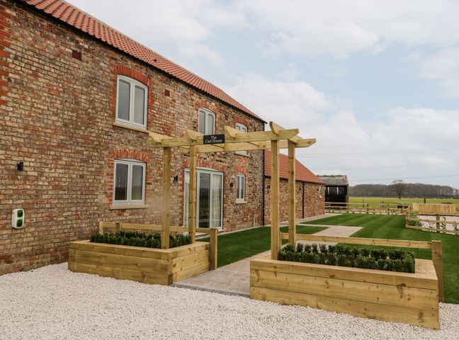 The exterior of a brick building with tiled roof and wooden planters with a pergola at The Cart House in Wilberfoss