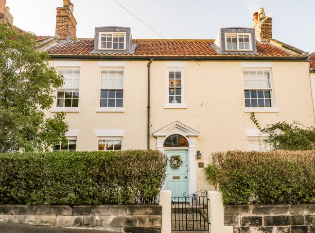 Front of a two-story house with a blue door and multiple windows behind a hedge at Stewart House in Whitby