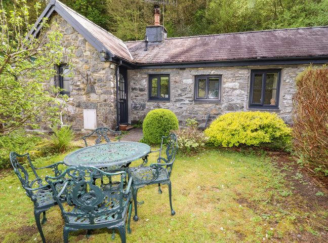 A stone cottage with a slate roof and a metal table with four chairs on a grass lawn at Tyn Y Ffynnon in Betws-Y-Coed