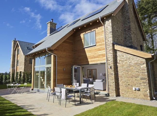 An outdoor patio with dining table and chairs next to a house with wooden and stone exterior at 3 The Drive Hillfield Village in Dartmouth