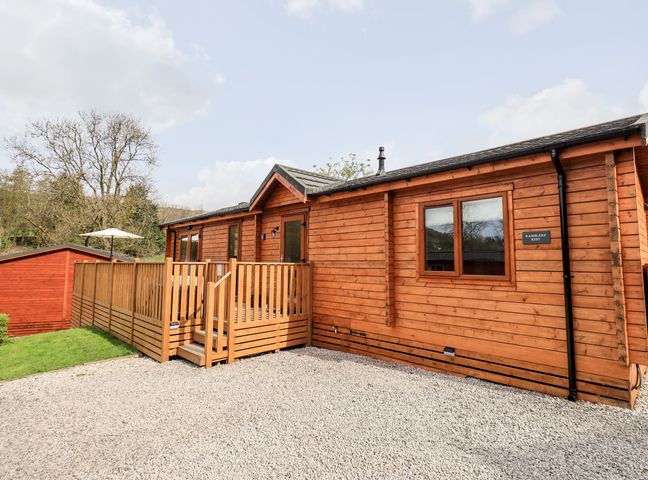 A wooden cabin with a fenced porch and gravel driveway at Ramblers Rest Lodge Pinewood 22 Limefitt Park near Windermere