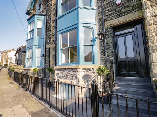 The exterior of a stone building with blue bay windows black door and black metal fence at The Haven in Windermere