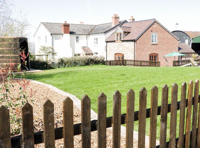A fenced garden with green grass next to a brick and a white house at The Cider House in Leominster