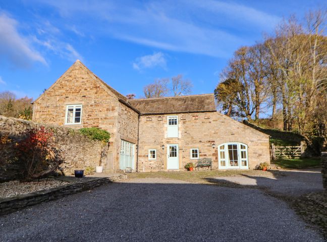 A stone house with multiple windows and a wooden bench outside at The Barn in Frosterley