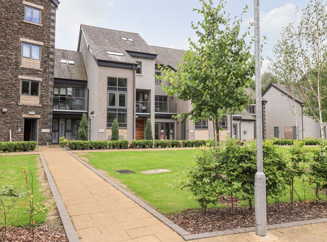 A pathway leading to modern apartment buildings with lawns and small trees at Rivers Edge in Newby Bridge