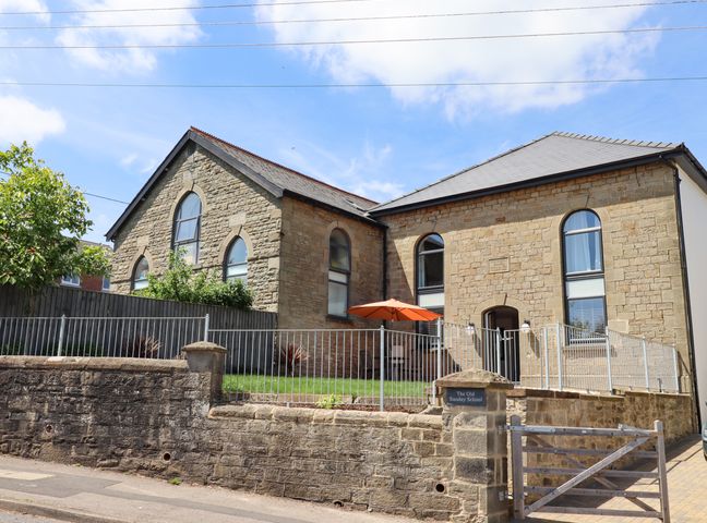 A stone building with arched windows and a fenced front yard with an orange umbrella at The Old Sunday School in Bream