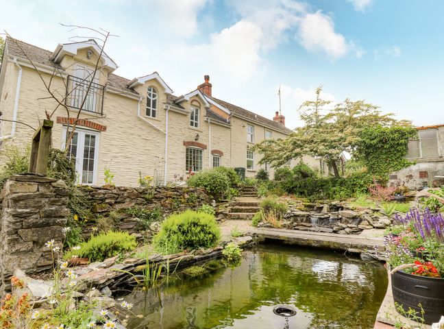 A stone house with plants and a pond in the garden at Spring Cottage in Pentre-Cwrt