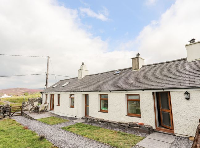 A white single-story house with gray roof and chimneys with a gravel path and green lawn at Penrallt Fawr in Rhosgadfan near Waunfawr