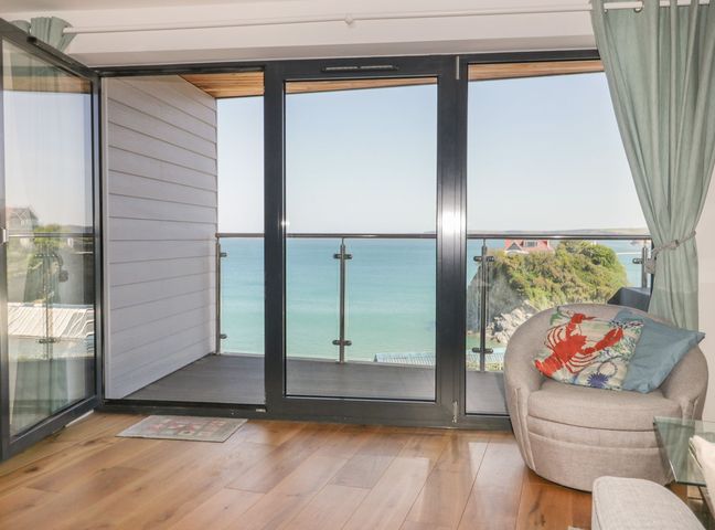 A room with wooden floor a round grey chair with cushions near glass doors opening to a balcony overlooking the sea at Onshore in Newquay