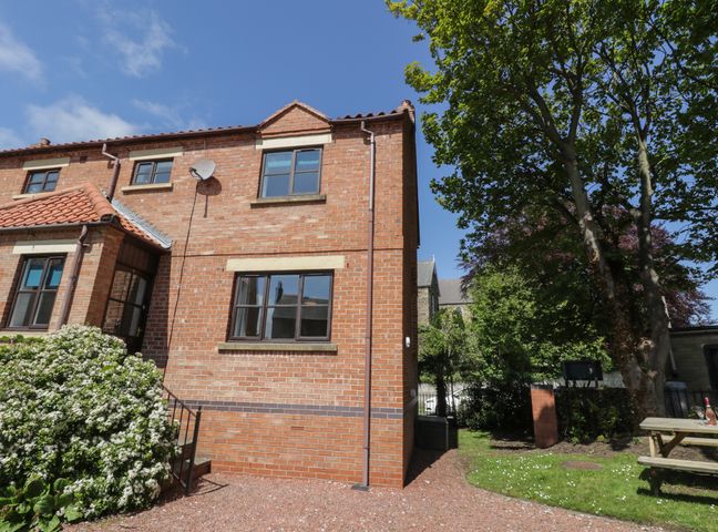 A brick house with windows and a small garden with trees and a picnic table at Dabbling Ducks in Ruswarp