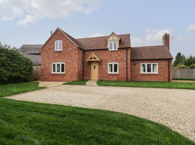 A brick house with multiple windows a wooden door and a gravel driveway surrounded by grass at Oakdene in Upper Quinton