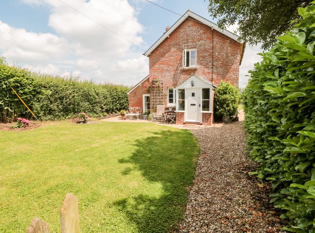 A brick house with a white door and windows surrounded by a lawn and gravel pathway at Old Rectory Cottage in Sturminster Newton