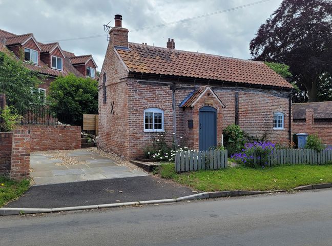 A brick cottage with a blue door a small garden and a paved driveway at Auld Cottage in Norwell