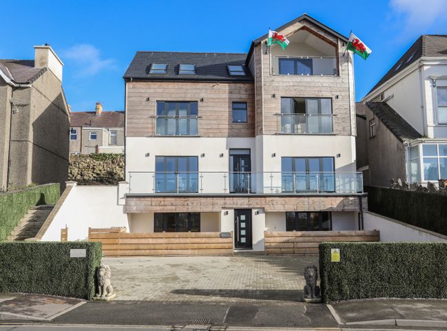 A multi-story building with glass balconies and two Welsh flags at Bryn Min Manton Penthouse Caernarfon