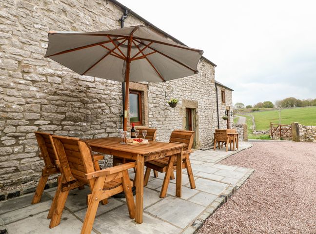 An outdoor patio area with wooden tables and chairs under umbrellas next to a stone building at Owls Barn in Coldeaton near Hartington