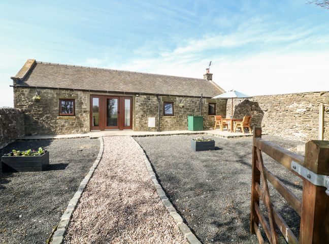 Exterior of a stone cottage with a gravel pathway leading to wooden doors and a patio table with chairs and umbrella at Shepherds Retreat in Coldeaton near Hartington