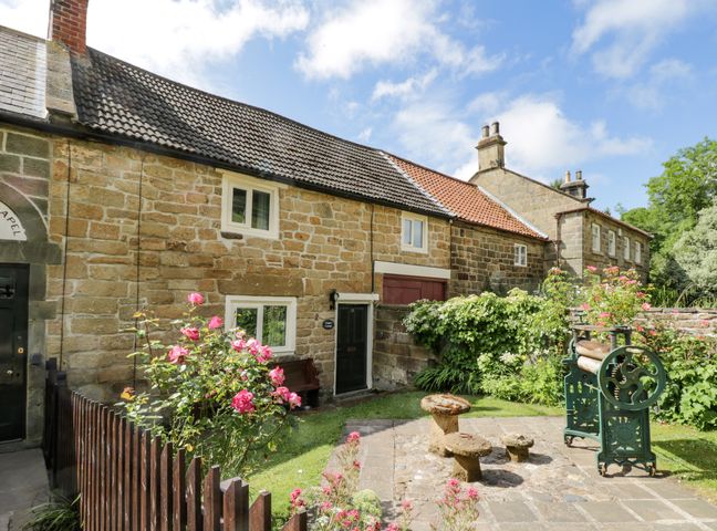 A stone cottage with flower bushes and garden equipment in a courtyard at Chapel Cottage in Upleatham near Saltburn-By-The-Sea