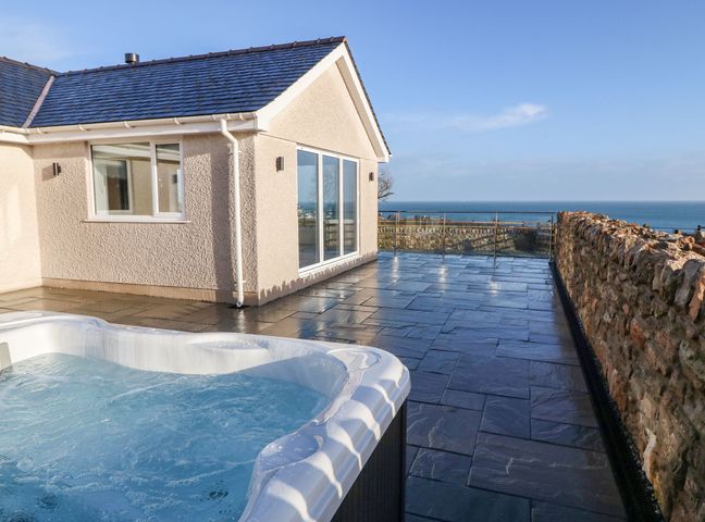 An outdoor patio with a hot tub stone wall and sea view at Yr Hen Feudy in Moelfre