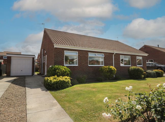 A brick bungalow with a tiled roof a driveway a garage and a lawn with bushes and flowers at Rose Bungalow in Whitby
