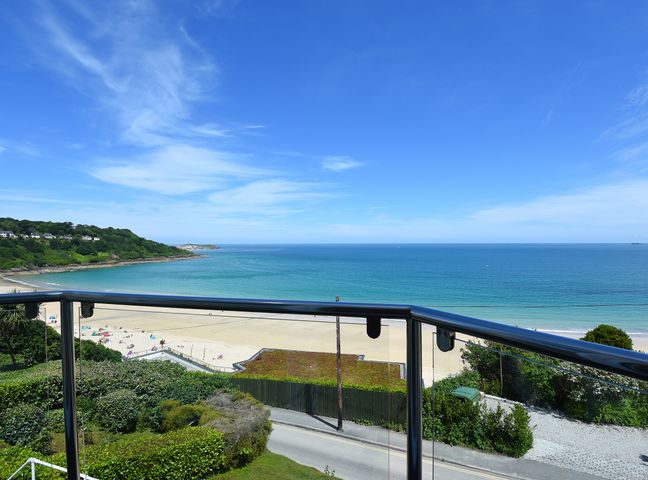 A beach with sand and people by the sea viewed from a balcony with railing at Treth Ha Mor in Carbis Bay