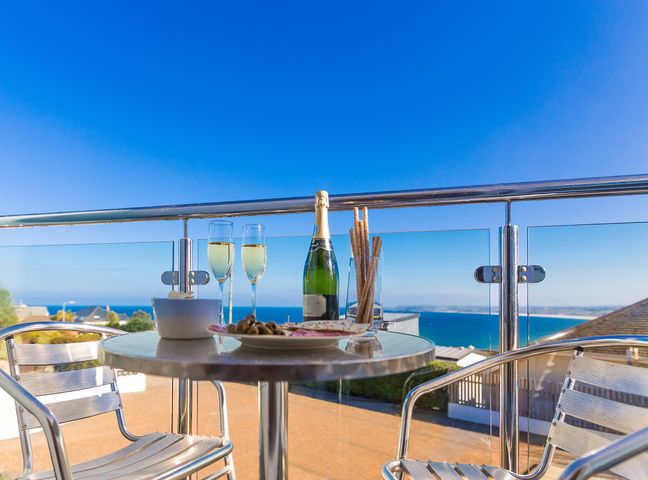 A balcony with a round table set with champagne, glasses, and snacks overlooking the sea at Genoa in Carbis Bay