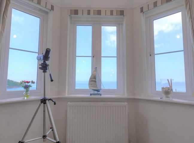 A room with three windows a telescope a model sailboat flowers in a vase and a glass container with shells at Golva in Carbis Bay
