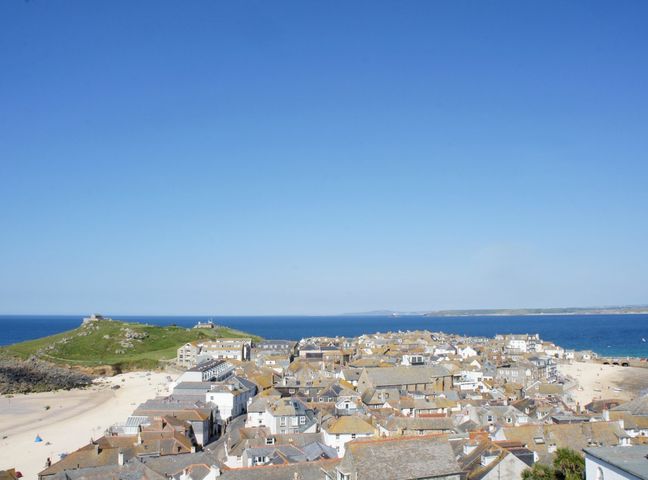 A coastal town with buildings and a beach next to a grassy hill by the sea at Prospect in St Ives