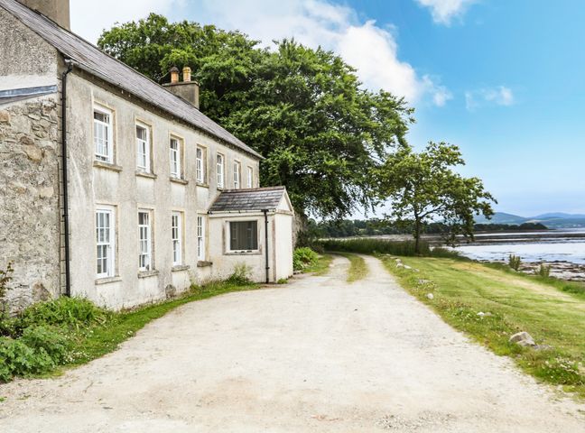 A gravel driveway beside a stone house near a body of water with trees and hills in the background at The Ferry House in Ramelton County Donegal