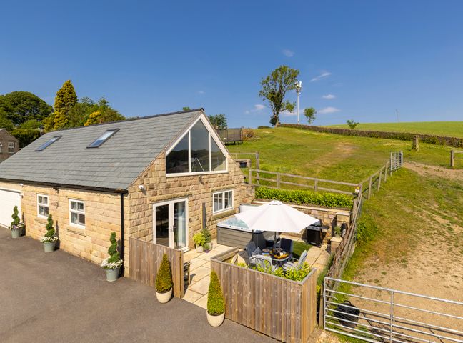 A stone cottage with a fenced patio area containing a table with chairs and an umbrella next to grassy fields at Walton House Cottage in Chapel-En-Le-Frith