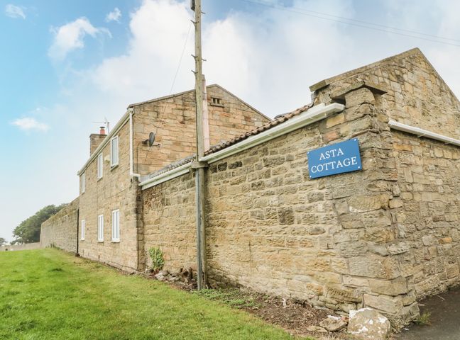 Stone exterior of a cottage with a blue sign reading Asta Cottage on a grassy area at Asta Cottage in Cresswell