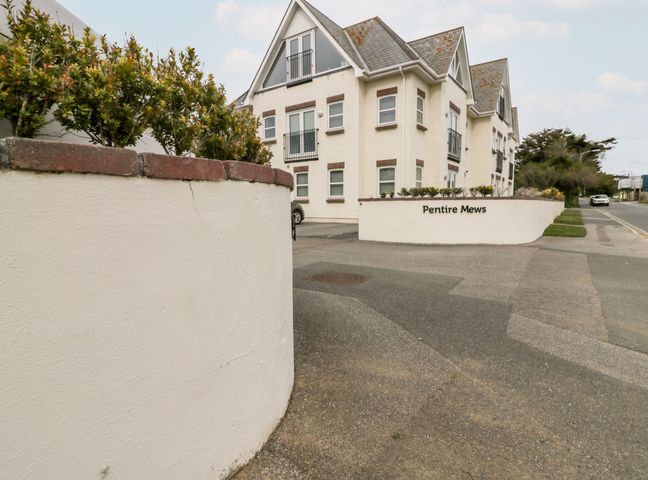 A street view of a white residential building with small balconies and a sign reading Pentire Mews with shrubbery on a low wall in Newquay