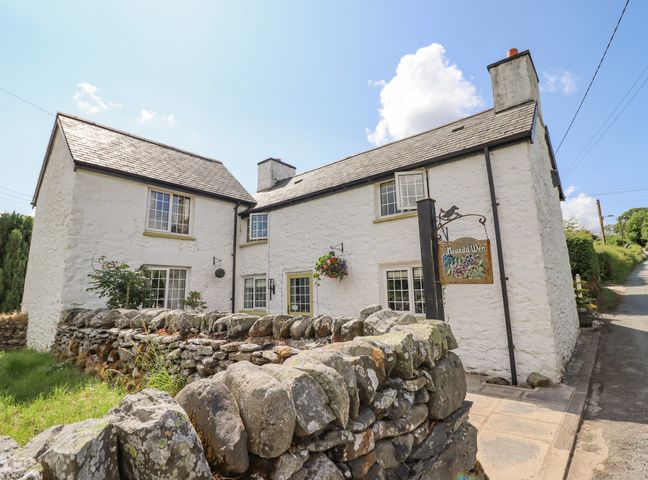 A white stone cottage with multiple windows and a stone wall in front at Neuadd Wen in Cerrigydrudion