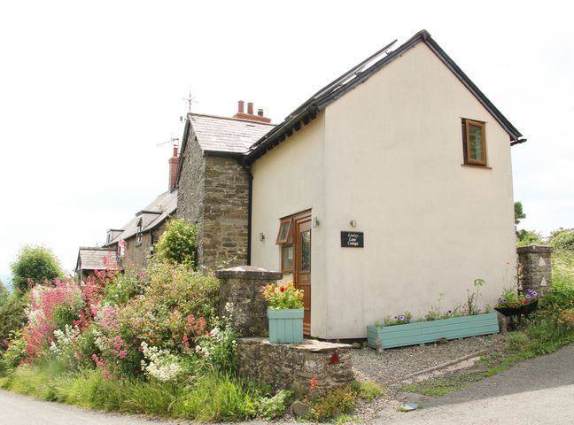 A cottage with stone and white walls surrounded by flowers and plants at Linley Lane Cottage Norbury near Bishops Castle