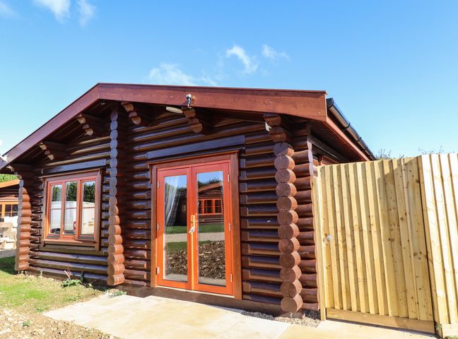 A wooden log cabin with double glass doors and a window next to a wooden fence at Pine Lodge in Greetham Rutland