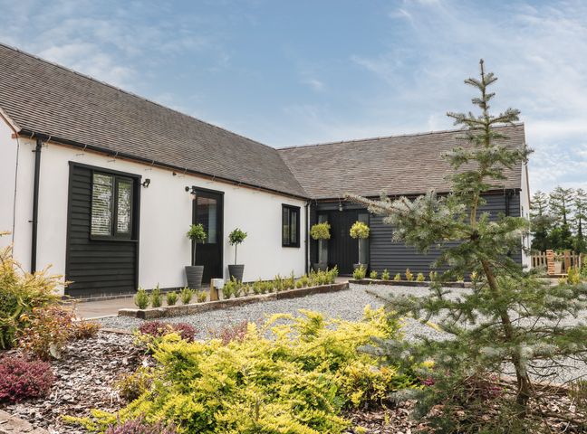A single story house with white and dark gray siding with a garden and small trees in front at The Den Bank Top Farm Roston near Ashbourne