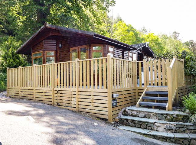 A wooden lodge with a fenced deck and steps surrounded by trees at Broad Oak Lodge in Applethwaite 7 Limefitt Park near Windermere