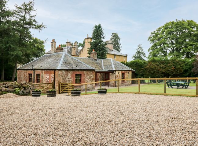 A small stone building with a slate roof surrounded by gravel and a fenced grassy area with outdoor seating at The Old Laundry Cottage in Aberargie near Perth