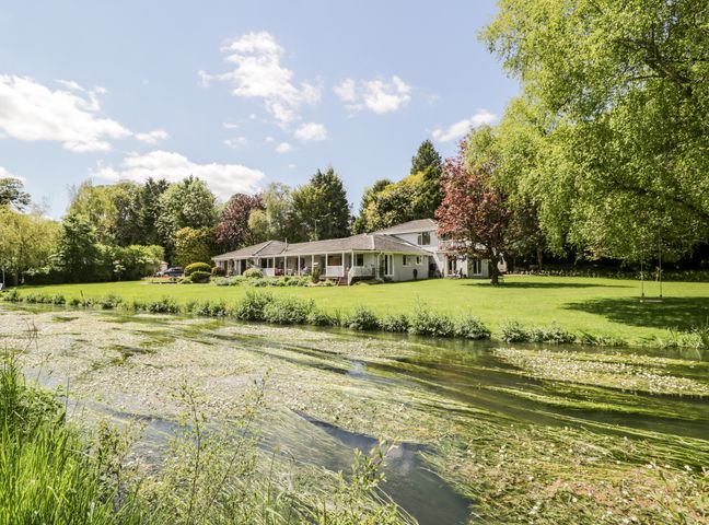 A house with a lawn and river in front surrounded by trees at The River House Avon Valley Stonehenge with fishing Salisbury