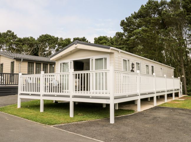A beige mobile home with a white railing deck surrounded by trees at The Rodley Pines in Cayton