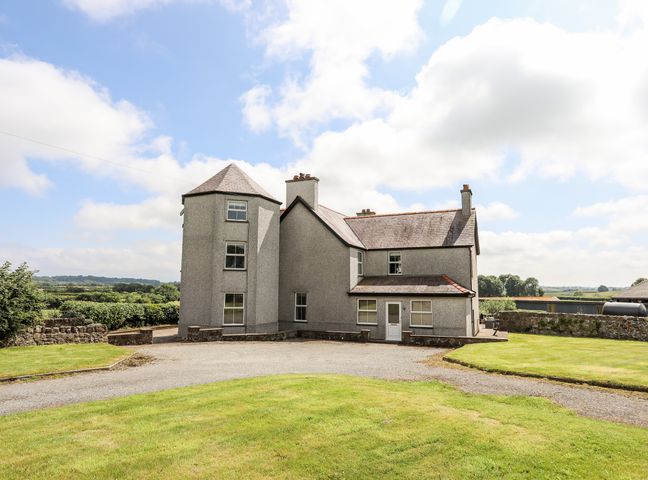 A large gray house with a tower and multiple chimneys surrounded by green lawns at Plas y Brain in Llanbedrgoch near Pentraeth