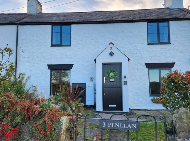 Exterior view of a white cottage with black framed windows and a black door with a wreath at 3 Penllan Cottages in Llanasa