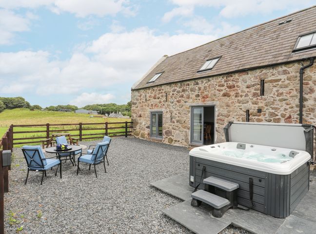 An outdoor patio with a hot tub and a seating area with four blue cushioned chairs at Gwel Y Fenai in Y Felinheli