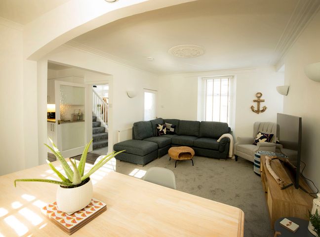 A living room with a sectional sofa a beige armchair a wooden coffee table and a flat screen TV at Sandpiper Cottage in Cullen