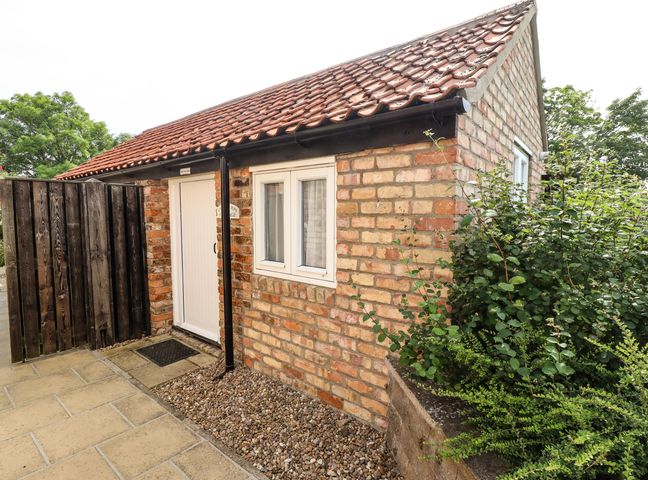 A small brick cottage with a tiled roof a white door and window next to a wooden fence and bushes at Cherry Pips in Saltfleetby