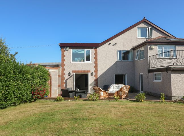 A backyard with outdoor seating and a two-story house with open windows at Plas Eithin in Mynydd Mechell near Llanfechell