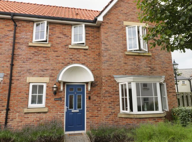 Front view of a brick house with a blue door and multiple windows at 2 Perran Court The Bay - Filey