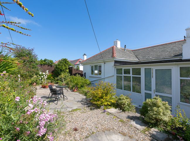 A garden area with gravel and plants with a small table and two chairs outside a white house at Brynmaur in Carbis Bay